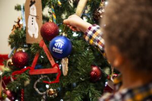 Boy places Habitat for Humanity ornament on Christmas tree. Donate unwanted holiday items and decorations.